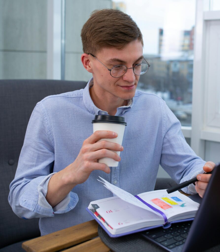Young man with eyeglasses enjoying a coffee break while working on a laptop at the office.